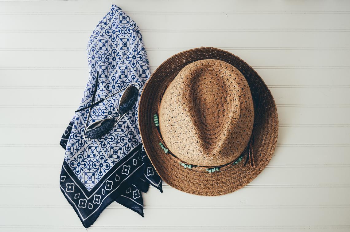 a straw hat, sunglasses and a blue bandana sit on a table