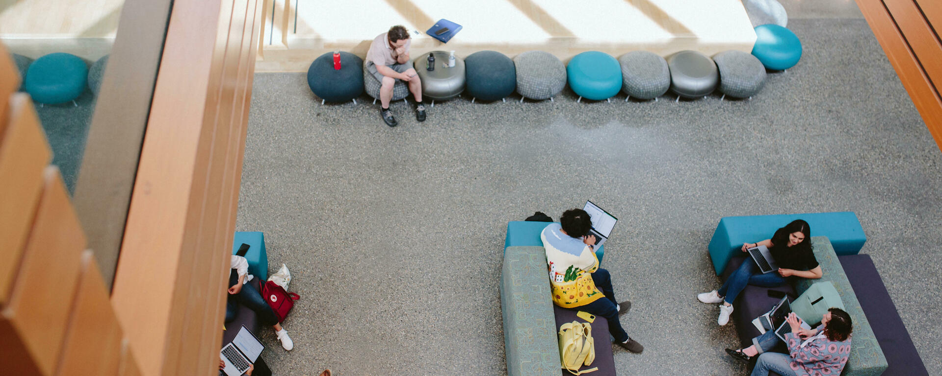 Students study in a sunny Taylor Institute atrium, on brightly coloured couches and poufs.