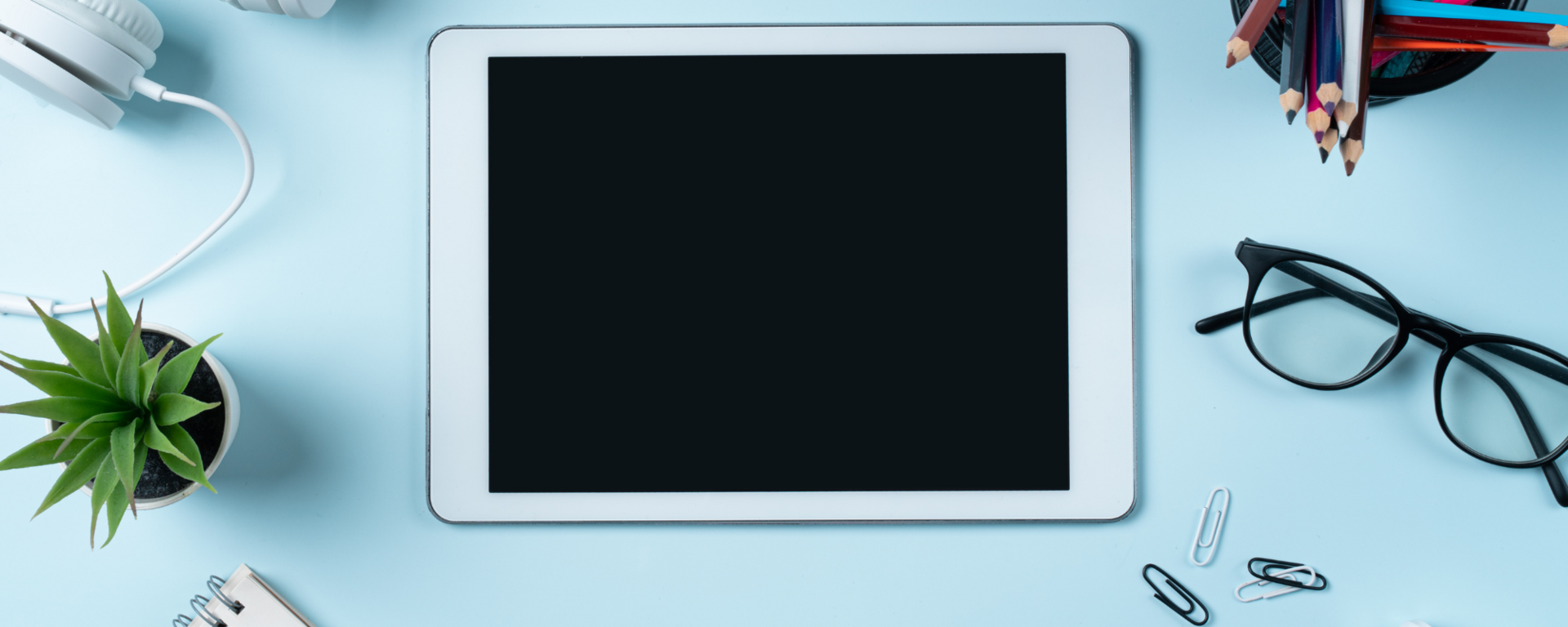 A tablet, a notepad, headphones and other learning modalities lie on a table