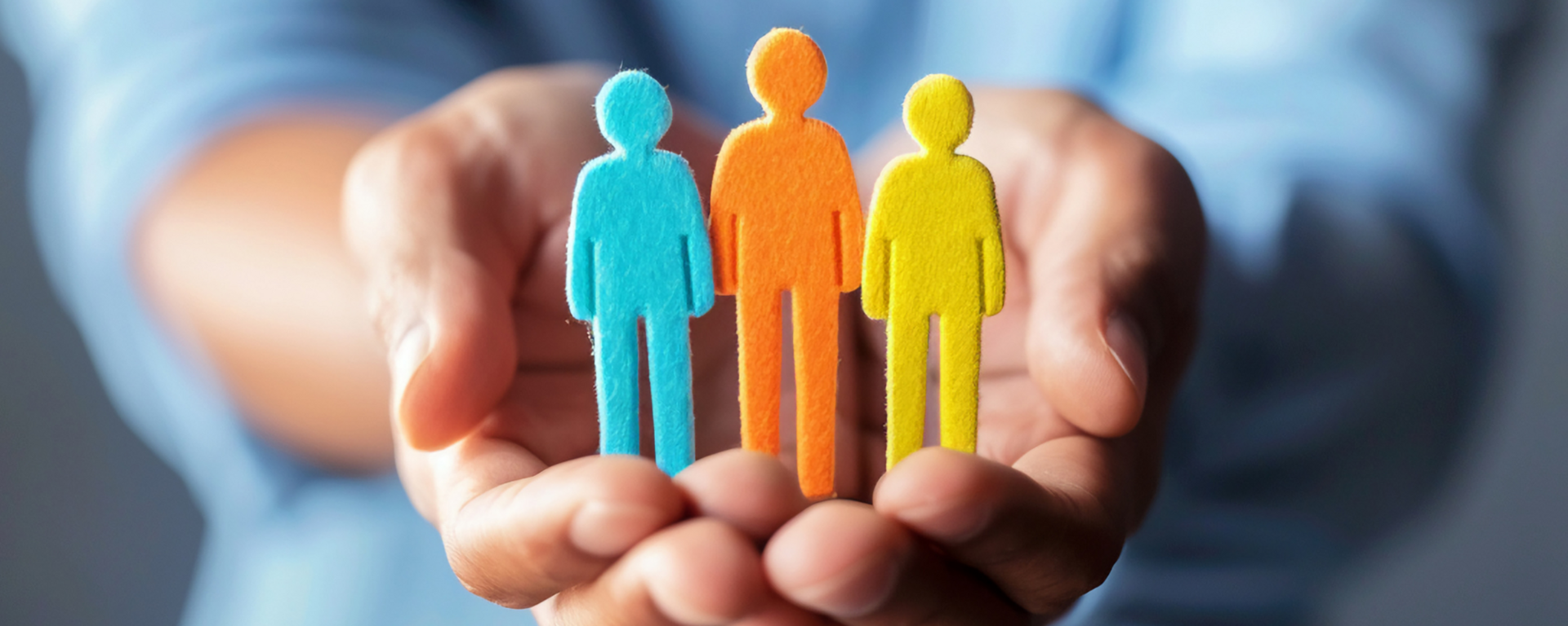 A pair of hands hold differently coloured felt statues of people