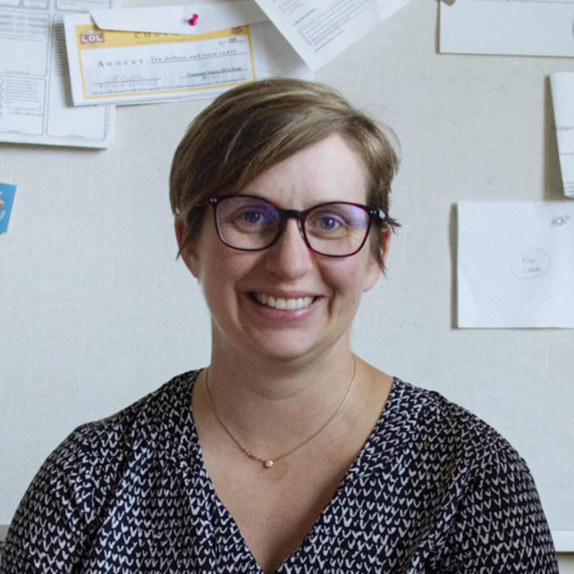 Lora Oelberg, a light-skinned woman with short brown hair and glasses, sits in an office.