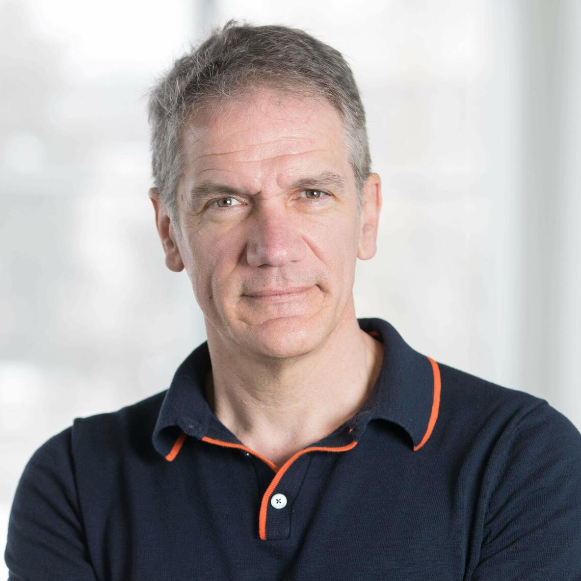 John Holash, a white man with grey hair, arms crossed looking forward.