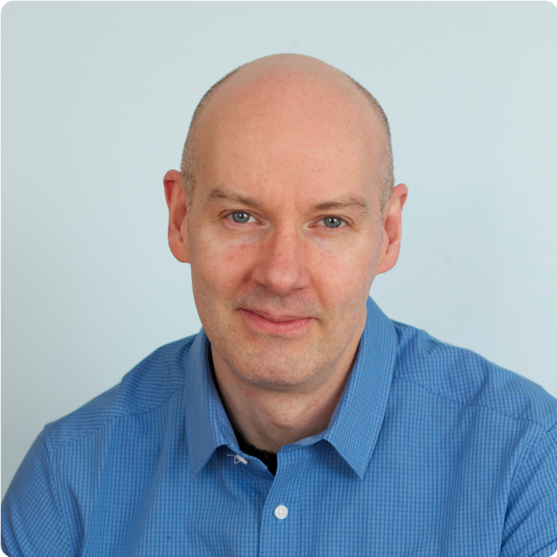 Neil Christensen, a bald, fair man wearing a blue collared shirt, looks ahead.