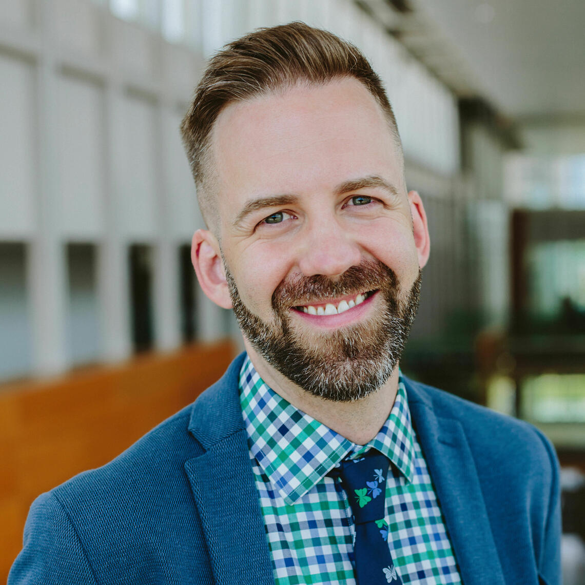 Derritt Mason, an educator with fair skin, short brown hair, and a salt-and-pepper beard, is wearing a blue blazer with a tie and button up shirt and smiling inside the Taylor Institute for Teaching and Learning.