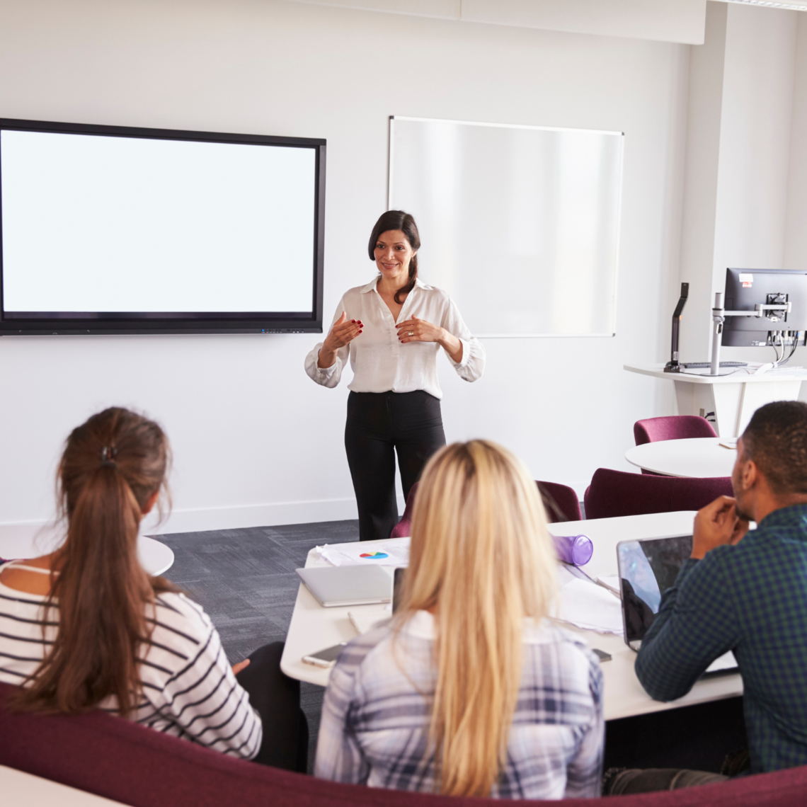 A female instructor delivers a lecture in front of a classroom of students