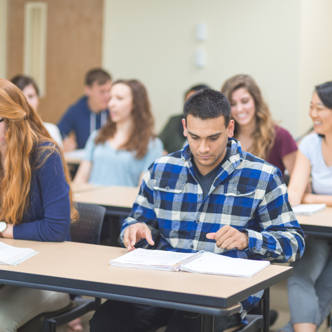 A male student looks down at his work in a full classroom