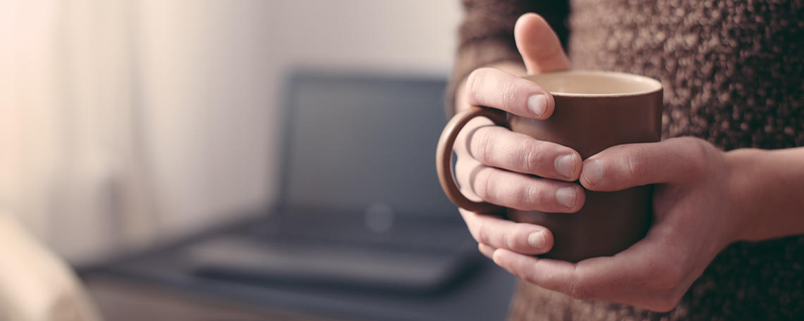 Hands holding a mug, person working from home