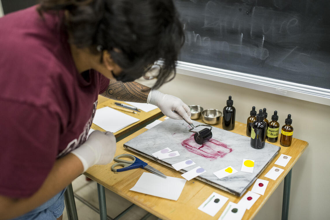 A student experiments with natural inks by rolling out ink on a slab for printing.