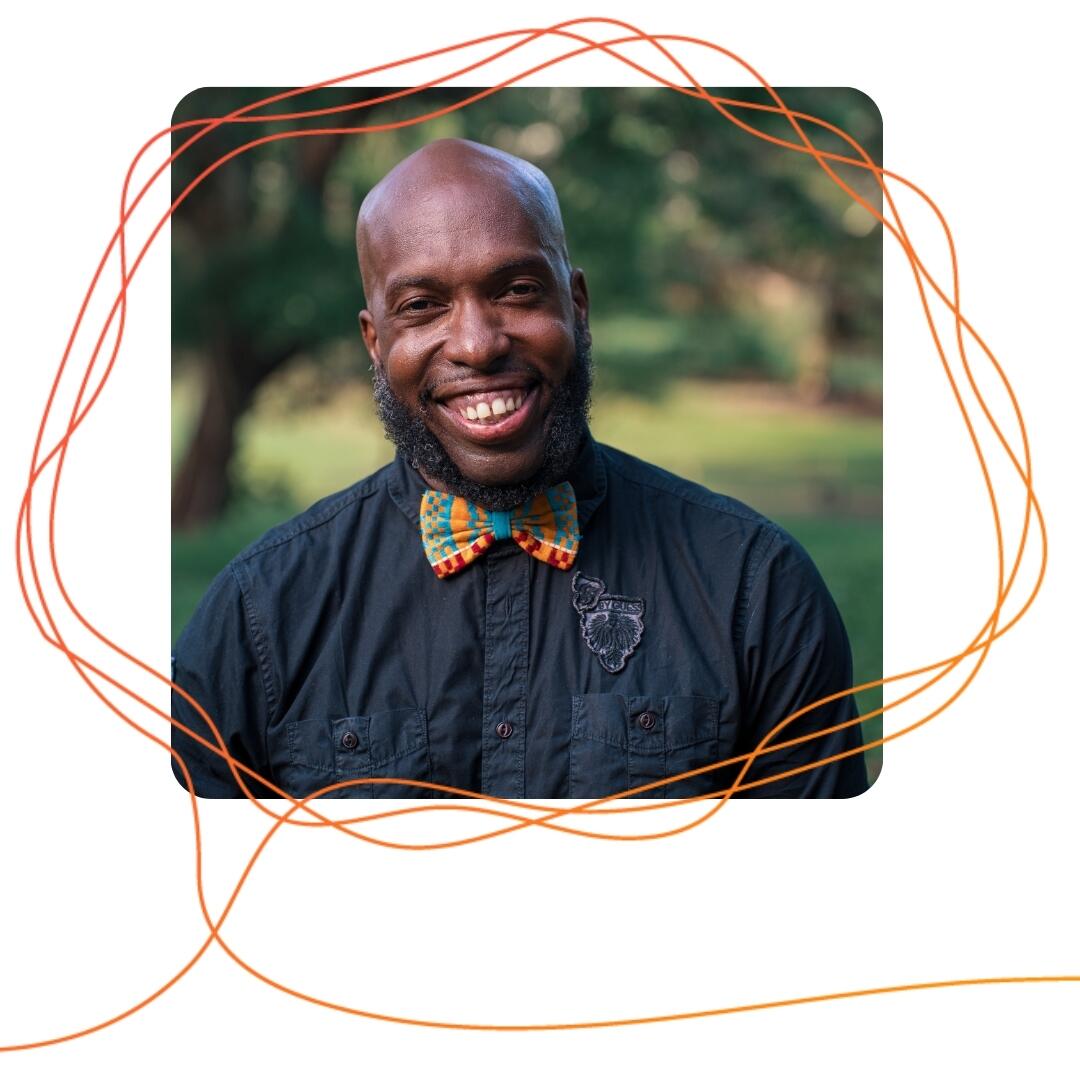 Bryan Dewsbury, a Black man wearing a bow tie, smiles with nature behind him.