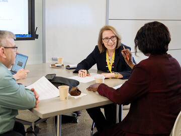 Three people sit at a table, engaged in discussion with oneanother
