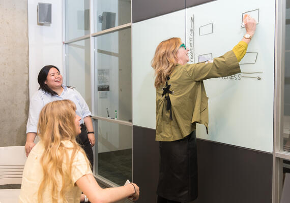 Dr. Cari Dinn draws on a whiteboard in a small classroom of students