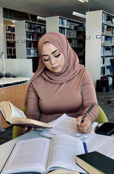 Photo of a student studying in a library with books across a table