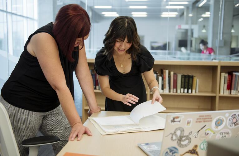 Katie Qin and professor look at book together