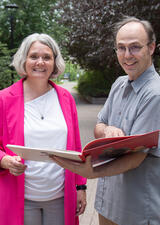 Roswita Dressler and John Scott stand outdoors holding a German children's book