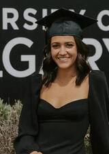 Megan Harmon stands in front of a UCalgary logo wearing a graduation cap