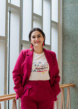 Mohaghegh Neyshabouri stands in front of a window in a red suit, smiling at the camera