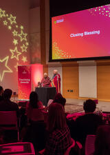 A speaker talks to an audience on a dimly lit stage at the Celebration of Teaching event. 