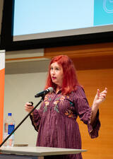 Dr. Kristen Gillespie-Lynch stands on stage at a conference speaking into a microphone
