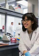 A student researcher in a labcoat sits in a science lab