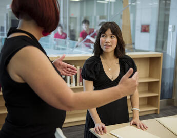 A supervisor and student talk in a library.