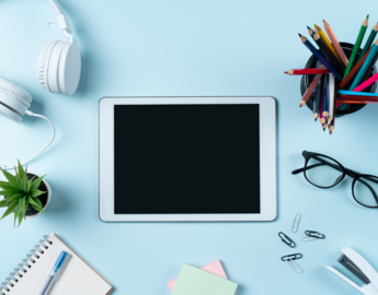 A tablet, a notepad, headphones and other learning modalities lie on a table
